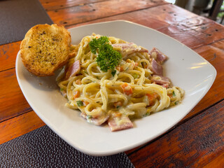 Spaghetti carbonara with ham and parsley on wooden table.