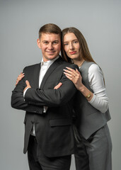 Business themed studio portrait of stylish young woman in pantsuit standing next to confident man in suit with crossed arms. Modern corporate fashion and team success concept.