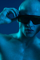A focused man wearing sunglasses, showcasing an intense expression, illuminated by blue lighting....