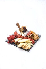 Gourmet charcuterie and cheese board on slate. Assorted cheeses, cured meats, fruits, nuts, and...