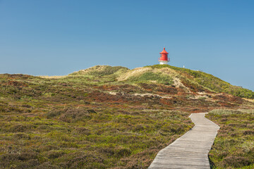 Wooden plank path through the dune landscape of Amrum, with the Quermarkenfeuer lighthouse in the background, Amrum, North Sea, North Frisian Islands, Schleswig-Holstein, Germany