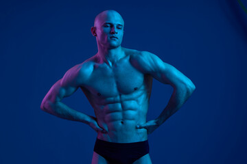 Athletic man posing confidently under dramatic blue lighting, showcasing a strong physique. This striking image highlights his muscular form in a unique light.