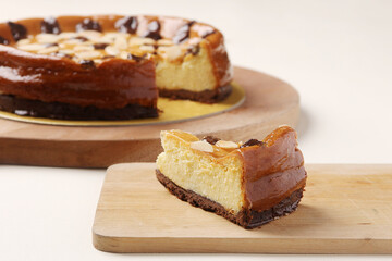 Slice of creamy baked cheesecake with almond slivers and chocolate chips, with the full cake in the background.