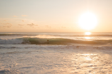 Surfer on a shortboard rides in a wave tube with the setting sun in the background. Surfer caught a wave in the ocean