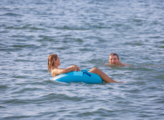 A guy swims up to a young girl floating on an inflatable circle