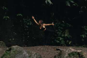 Naklejka premium Woman stretching in yoga pose near rainforest rock formation