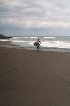 Surfer walking along black sand beach under moody skies