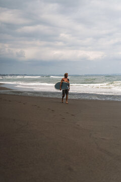 Surfer walking along black sand beach under moody skies