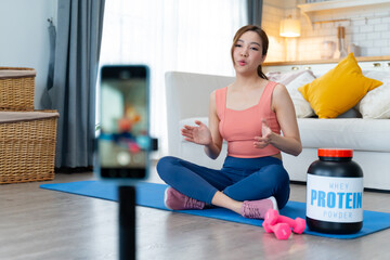 Young attractive woman in athletic wear sits on yoga mat and drinking protein powder milkshake after workout at fitness gym,smiling at her whey protein shake.Diet meal replacement for weight loss.