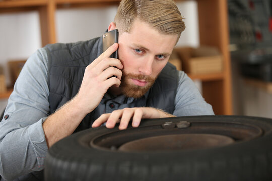 mechanic looking at tyre and making call on smartphone
