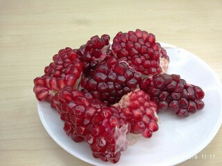 Juicy, deep red pomegranate arils displayed on a white plate