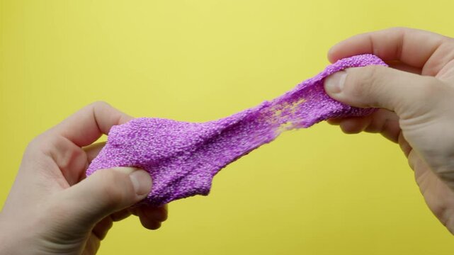Pink Floam slime is slowly kneaded for ASMR against a vibrant yellow background, creating satisfying sounds.