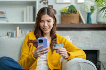 Asian woman shopping online at home with credit card and mobile phone.Happy Asian female sitting on...