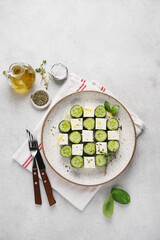 Stylish serving of cucumber and feta cheese salad on ceramic plate on napkin on white background. vegetarian cuisine. top view