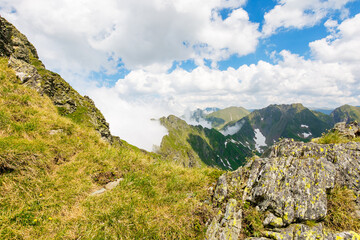 alpine landscape of romania in summer. rocky scenery. fagaras mountain ridge on a sunny day. scenic valley with snow on the grassy slope beneath a blue sky with clouds. travel to transylvania
