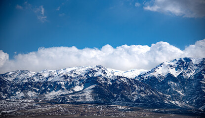 The image shows a majestic mountain range covered in snow under a dramatic sky filled with large,...