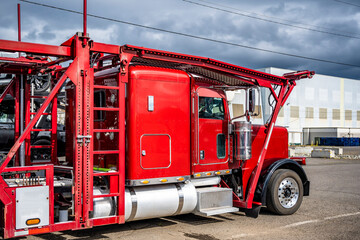 Bright red big rig car hauler semi truck with empty modular semi trailer standing on the industrial...