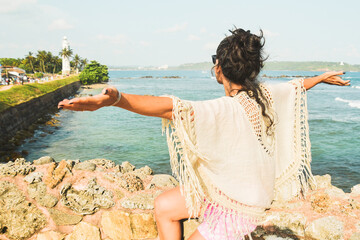 Woman tourist sit arms outstretched enjoy panoramic Lookout from UNESCO Galle Fort. Galle Fort Walk with Ocean Views concept. Sightseeing landmark and popular visit destination in Sri lanka