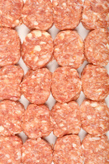 A close-up, overhead shot shows a group of raw savory minced meat and cheese patties filling the frame, displaying their texture