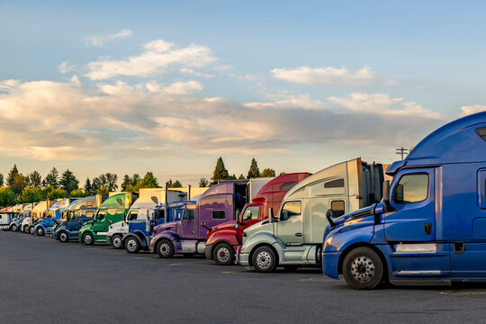 Professional carriers big rig semi trucks with semi trailers standing in row on truck stop parking lot taking a break