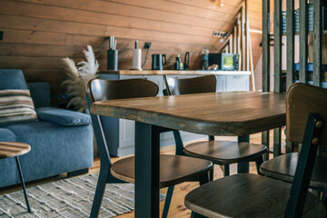 Close-up of modern wooden dining table and chairs in cozy Scandinavian style kitchen with wooden walls, blue sofa, and kitchen countertop