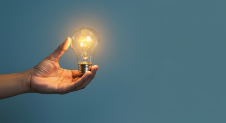 Hands gently holding a light bulb that glows with warm light and minimal background, copyright