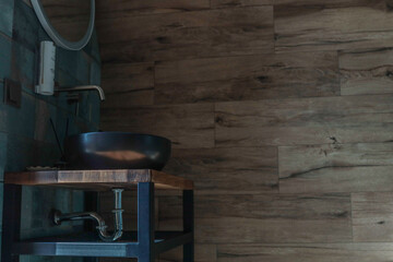 Minimalist bathroom interior with round black sink, wooden countertop, tiled wall, and wood-paneled wall, featuring modern design elements