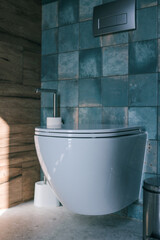 Minimalist wall-mounted toilet with blue ceramic tiles, wooden accent wall, and stainless steel...