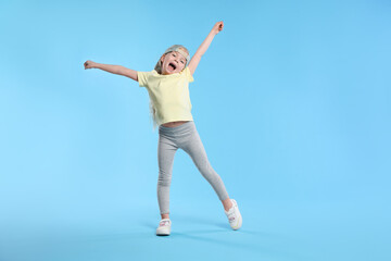 Obraz premium Cute little girl dancing on light blue background, space for text