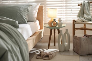 Comfortable bed with soft linens, lamp and decor in stylish room. Home textile