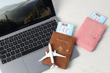 Passports, flight tickets, plane model and laptop on white wooden table, above view