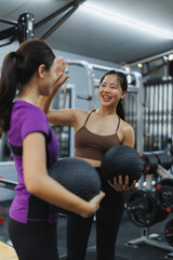 Two young women giving high five holding medicine balls in the gym