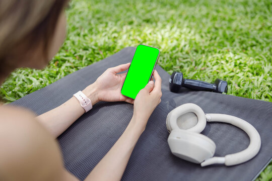 A serene moment captured in nature where an individual engages with their smartphone while surrounded by fitness gear on a yoga mat amidst a lush green backdrop of grass.