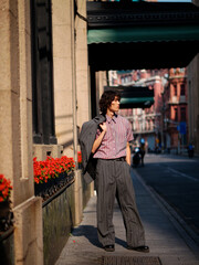 Portrait of handsome Chinese young man wearing gray suit posing in the street, young guy with black curly hair with urban background. Male fashion, cool Asian young man lifestyle.