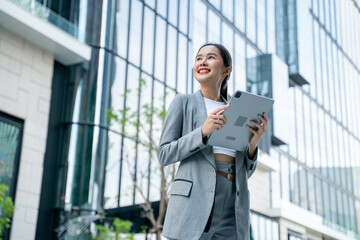 Young adult business working asian woman using digital tablet for online application on day.Asia Business female standing or walking on big city urban street outside.City Streets With People concept