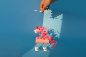Handmade pink unicorn marionette toy crafted from cardboard tube, yarn, and plastic caps on blue...