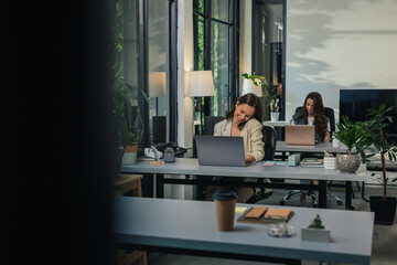 Young businesswoman talking on phone and working on laptop in modern office