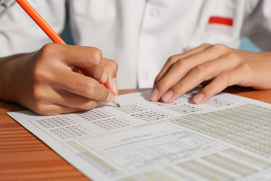 Close-up of an Indonesian student filling out a multiple choice answer sheet with a pencil during an academic exam. No face visible.