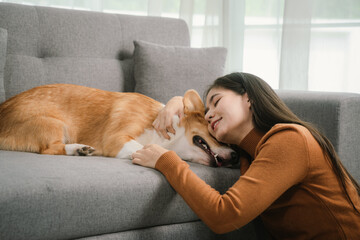 A cheerful young woman sits at home on a comfortable sofa, happily hugging her cute dog in a warm and loving home.