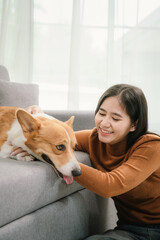 A cheerful young woman sits at home on a comfortable sofa, happily hugging her cute dog in a warm and loving home.