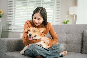A cheerful young woman sits at home on a comfortable sofa, happily hugging her cute dog in a warm and loving home.
