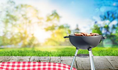 charcoal barbecue grill with open flame, chicken meat, backyard and wooden table with red tablecloth