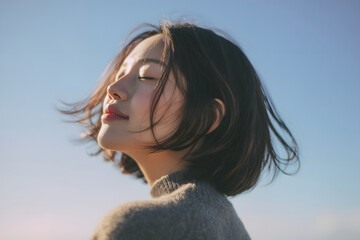 風に髪をなびかせて微笑む若い日本人女性のアップポートレート