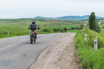 Motorcyclists travel along a rural mountain road in the Chui region of Kyrgyzstan.