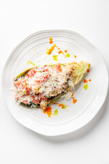 Grilled romaine lettuce salad topped with diced tomatoes, shredded cheese, and herbs, drizzled with vibrant orange and green sauces, served on a white plate.