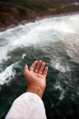 Female hand reaching out above ocean water with splash in sunlight under clear blue sky