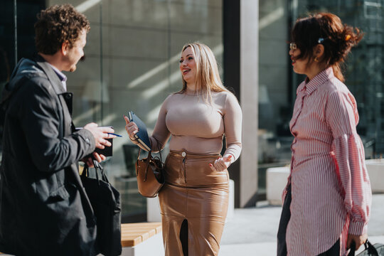 Business colleagues engage in a lively conversation outside a modern office building, enjoying a sunny day. The group appears friendly and professional, reflecting business and communication concepts.