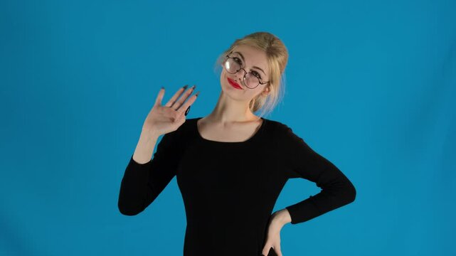 Smiling lady lifts hand from waist welcomingly waving at camera. Lowering palm pretty female model questioningly raises left eyebrow slow motion