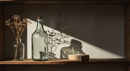 Glass bottles and dried flowers casting shadows on wooden shelf  