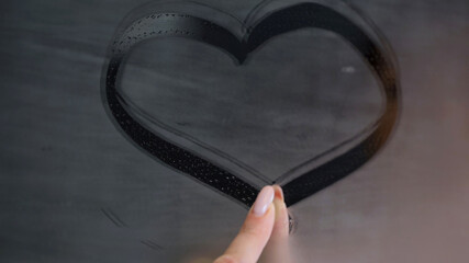 Woman finger glides over fogged glass leaving heart on window